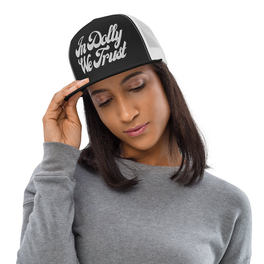 Black trucker cap with white cursive In Dolly We Trust lettering and white mesh back.